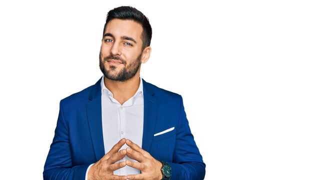 Young hispanic man wearing business jacket hands together and fingers crossed smiling relaxed and cheerful. success and optimistic