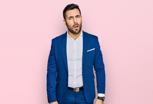 Young hispanic man wearing business jacket in shock face, looking skeptical and sarcastic, surprised with open mouth