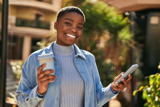 Young african american woman using smartphone and drinking coffee at the city