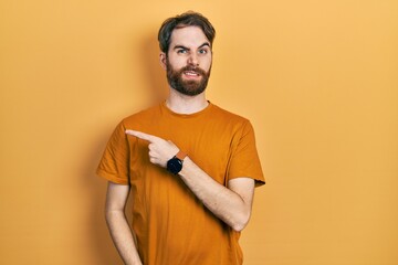 Caucasian man with beard wearing casual yellow t shirt pointing aside worried and nervous with...