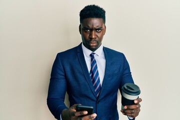Handsome business black man using smartphone and drinking a cup of coffee skeptic and nervous, frowning upset because of problem. negative person.