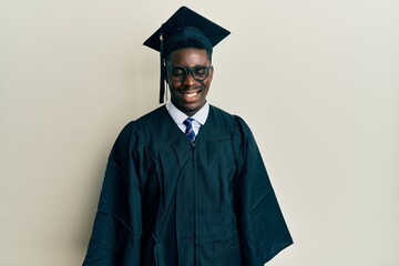 Handsome black man wearing graduation cap and ceremony robe winking looking at the camera with sexy...
