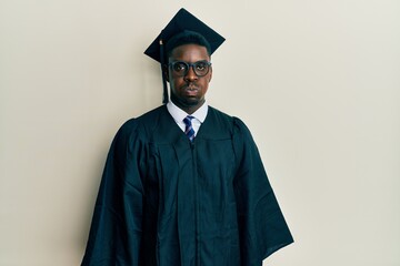 Handsome black man wearing graduation cap and ceremony robe puffing cheeks with funny face. mouth inflated with air, crazy expression.