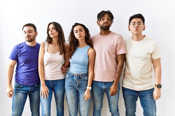 Group of young people standing together over isolated background looking at the camera blowing a kiss on air being lovely and sexy. love expression.