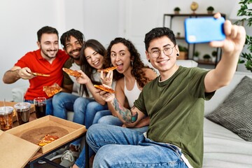 Group of young friends smiling happy eating italian pizza make selfie by the smartphone at home.