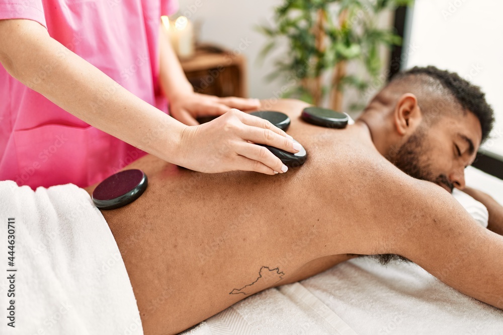 Sticker Man reciving back massage with black stones at beauty center.