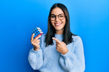 Young brunette woman playing colorful puzzle cube intelligence game smiling happy pointing with hand and finger