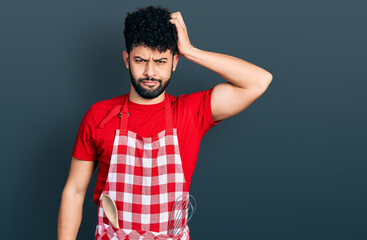 Young arab man with beard wearing cook apron confuse and wonder about question. uncertain with doubt, thinking with hand on head. pensive concept.