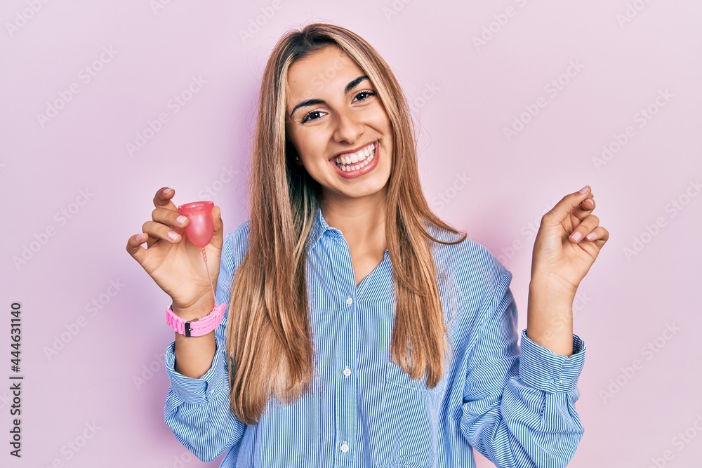 Sticker Beautiful hispanic woman holding menstrual cup smiling happy pointing with hand and finger to the side