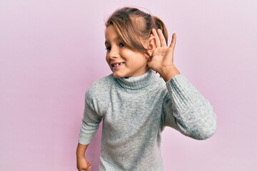Little beautiful girl wearing casual turtleneck sweater smiling with hand over ear listening and hearing to rumor or gossip. deafness concept.