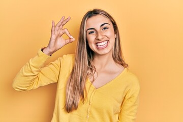 Fototapeta premium Beautiful hispanic woman wearing casual yellow sweater smiling positive doing ok sign with hand and fingers. successful expression.