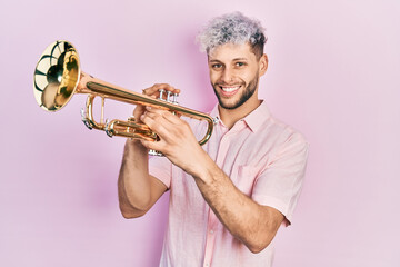 Young hispanic man with modern dyed hair playing trumpet smiling with a happy and cool smile on...