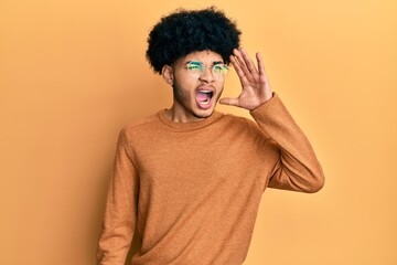 Obraz na płótnie Canvas Young african american man with afro hair wearing casual winter sweater shouting and screaming loud to side with hand on mouth. communication concept.