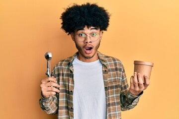 Young african american man with afro hair holding ice cream and ice cream scoop afraid and shocked...