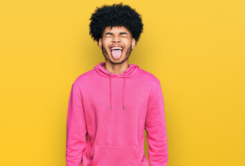 Fototapeta na wymiar Young african american man with afro hair wearing casual pink sweatshirt sticking tongue out happy with funny expression. emotion concept.