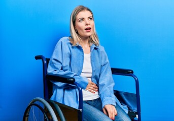 Beautiful caucasian woman sitting on wheelchair with hand on stomach because nausea, painful...