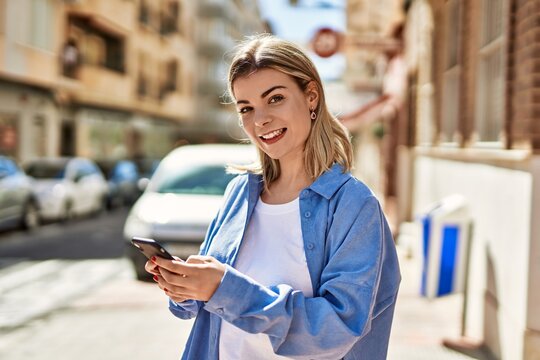 Young blonde girl smiling happy using smartphone at the city.