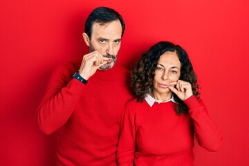 Middle age couple of hispanic woman and man hugging and standing together mouth and lips shut as...