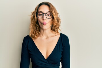 Young caucasian woman wearing business shirt and glasses making fish face with lips, crazy and...