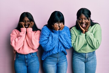 Three young african american friends wearing wool winter sweater laughing and embarrassed giggle...