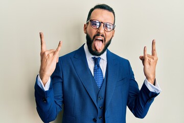 Young man with beard wearing business suit and tie shouting with crazy expression doing rock symbol with hands up. music star. heavy concept.