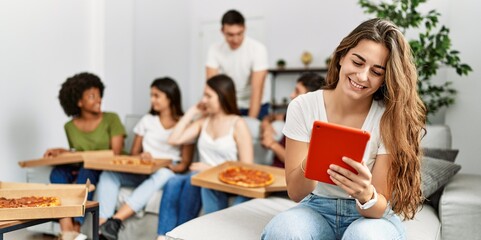 Group of young friends eating italian sitting on the sofa. Woman smiling and using touchpad at home.