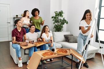 Group of young friends eating pizza and playing draw game at home.