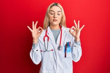 Young caucasian woman wearing doctor uniform and stethoscope relax and smiling with eyes closed doing meditation gesture with fingers. yoga concept.