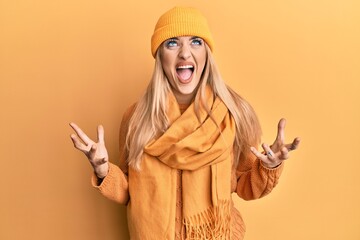 Young caucasian woman wearing wool winter sweater and cap crazy and mad shouting and yelling with aggressive expression and arms raised. frustration concept.