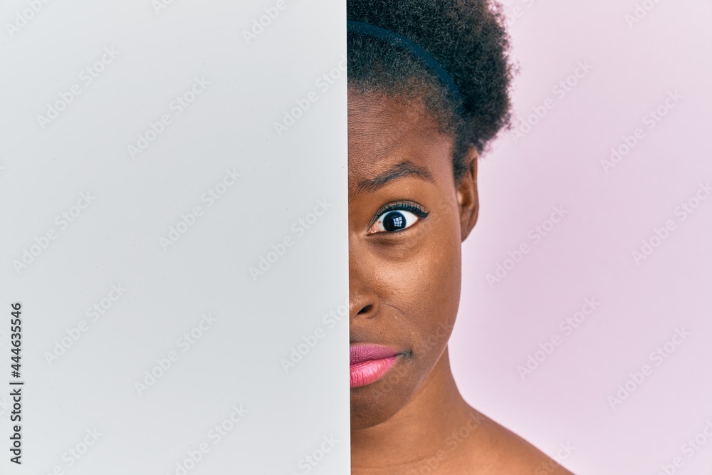 Poster Young african american girl holding blank empty banner over half face in shock face, looking skeptical and sarcastic, surprised with open mouth