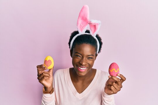 Young african american girl wearing cute easter bunny ears holding painted eggs smiling and laughing hard out loud because funny crazy joke.