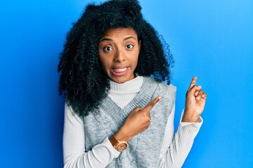 African american woman with afro hair wearing casual winter sweater pointing aside worried and...