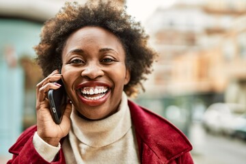 Beautiful business african american woman with afro hair smiling happy and confident outdoors at the city having a conversation speaking on the phone