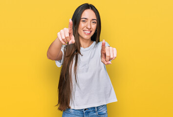 Young hispanic girl wearing casual white t shirt pointing to you and the camera with fingers, smiling positive and cheerful