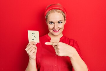 Young blonde woman holding dollar symbol reminder paper smiling happy pointing with hand and finger