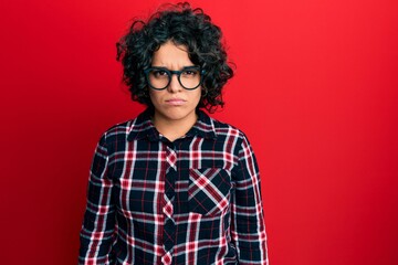 Young hispanic woman with curly hair wearing casual clothes and glasses skeptic and nervous, frowning upset because of problem. negative person.