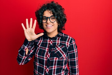 Young hispanic woman with curly hair wearing casual clothes and glasses showing and pointing up with fingers number five while smiling confident and happy.