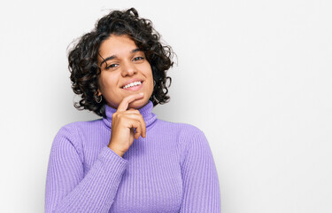 Fototapeta na wymiar Young hispanic woman with curly hair wearing casual clothes looking confident at the camera smiling with crossed arms and hand raised on chin. thinking positive.