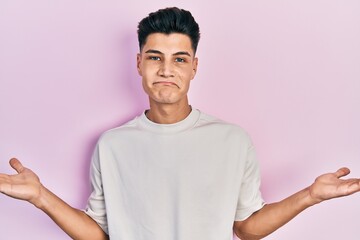 Young hispanic man wearing casual white t shirt clueless and confused with open arms, no idea and doubtful face.