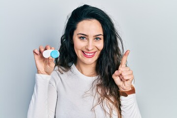 Young hispanic woman holding contact lenses smiling with an idea or question pointing finger with...