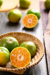 Green tangerine orange fruit in a bamboo basket on wooden background