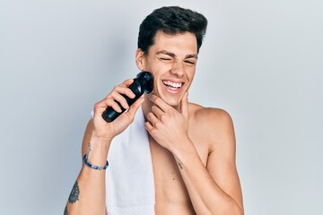 Young hispanic man shaving with electric razor machine winking looking at the camera with sexy...