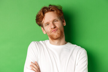 Emotions and fashion concept. Close-up of skeptical young man with red hair and beard pucker lips,...