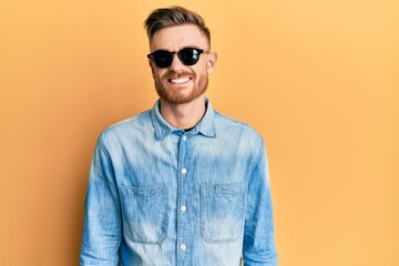 Young redhead man wearing stylish sunglasses looking positive and happy standing and smiling with a confident smile showing teeth