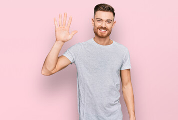 Young redhead man wearing casual grey t shirt showing and pointing up with fingers number five while smiling confident and happy.