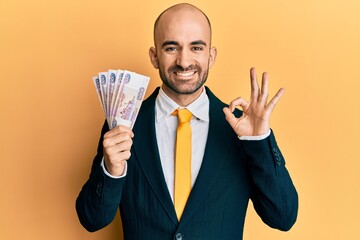 Young hispanic business man holding russian 500 ruble banknotes doing ok sign with fingers, smiling friendly gesturing excellent symbol