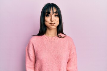 Young brunette woman with bangs wearing casual winter sweater puffing cheeks with funny face. mouth inflated with air, crazy expression.