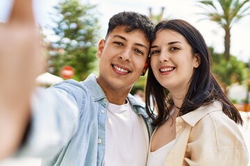 Young hispanic couple of boyfriend and girlfriend together outdoors on a sunny day, smiling in love taking a selfie picture