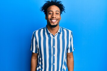 Young african american man with beard wearing casual striped shirt with a happy and cool smile on...