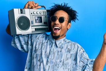 Young african american man with beard holding boombox, listening to music celebrating achievement with happy smile and winner expression with raised hand